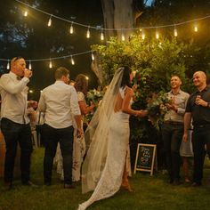 a bride and groom are standing under string lights