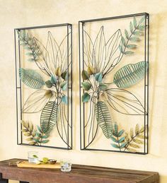 two metal wall art pieces with green leaves on them, hanging above a wooden table