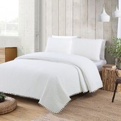 a bed with white sheets and pillows in a room next to a wooden wall on the floor