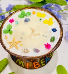 a bowl filled with white liquid surrounded by sea shells and flowers on top of a table