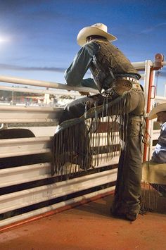 a cowboy leaning against a fence with his hat on