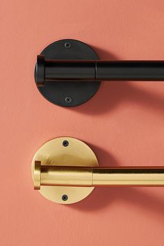 two black and gold door handles on a pink wall next to a pair of brass pulls