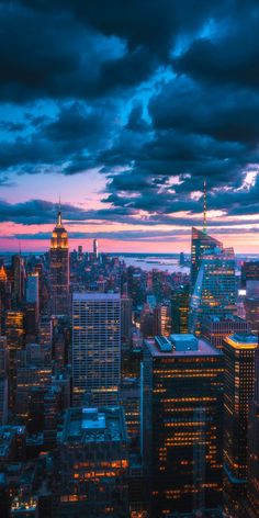 the city skyline is lit up at night, with clouds in the sky above it