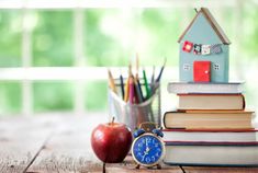 an alarm clock sitting on top of a stack of books next to an apple and pencils