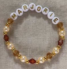 a beaded bracelet with the word marjorie written in white and gold beads