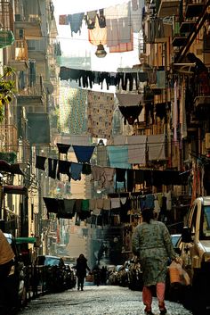 a man walking down a street next to cars and laundry hanging from the line above