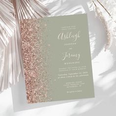 a wedding card with gold glitter on the front and silver foil on the back, sitting next to palm leaves