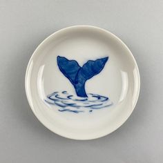 a blue and white plate with a whale tail on it's side in the water