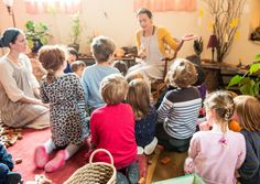 a group of children sitting on the floor in front of a woman talking to them