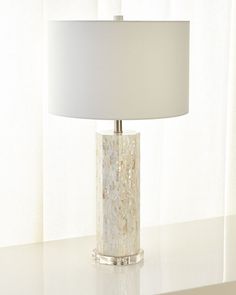 a white lamp sitting on top of a table next to a window covered in curtains