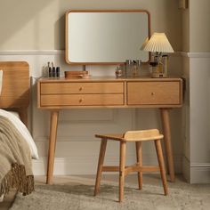 a wooden desk with a mirror, stool and lamp on top of it in front of a bed