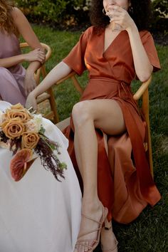 two women sitting on chairs in the grass eating food and drinking wine from their glasses