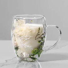 a glass cup filled with white flowers and greenery