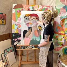 a man with dreadlocks standing in front of an art work on easel