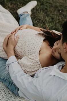 a man and woman are laying on the grass with their arms wrapped around each other