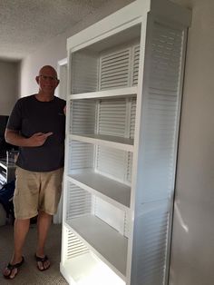 a man standing next to a tall white bookcase in an office building with his hand on the bottom shelf