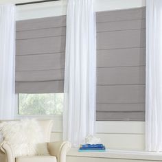 a white chair sitting in front of two windows with roman shades on the windowsill