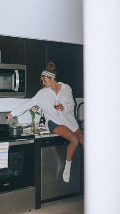 a woman sitting on top of a kitchen counter next to a stove and microwave oven