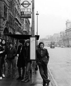 a group of people standing on the side of a road next to a bus stop