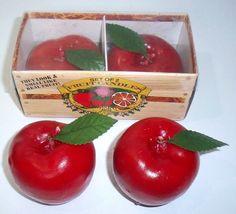 two red apples in a wooden box next to another one with green leaves on it