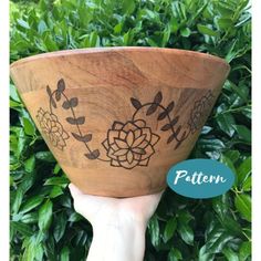 a hand holding up a wooden bowl with designs on it's sides and the bottom