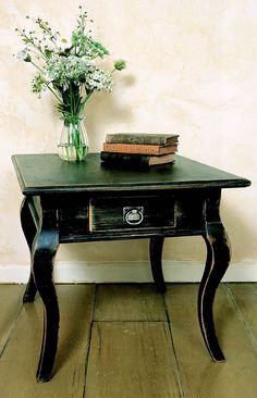 a black table with flowers and books on it next to a vase filled with white flowers