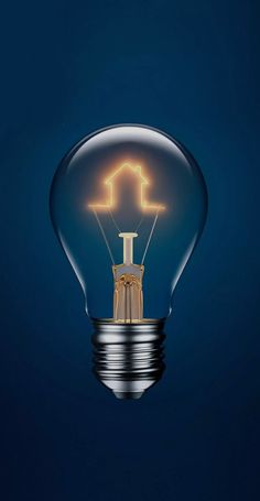 a light bulb with a house inside it on a dark blue background that is lit up in the shape of an arrow