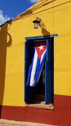 a flag is hanging in the open door of a yellow building with red, white and blue stripes