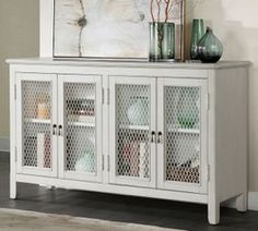 a white sideboard with glass doors and vases on top in a living room