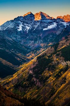 the mountains are covered in snow and fall colors as the sun is setting on them