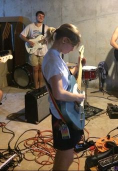 a group of young people playing instruments in a room with sound equipment on the floor