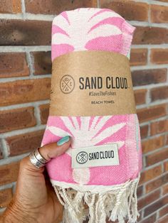 a hand holding up a pink and white towel with the words sand cloud on it