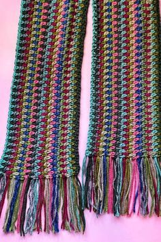 a pair of multicolored knitted scarves with fringes on pink background