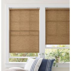 a living room with two windows covered in roman shades and striped pillows on the couch