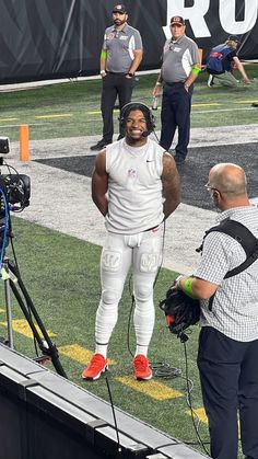 a football player standing on top of a field next to a cameraman and another man