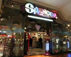 a store front with people standing in the doorway and on the sidewalk below it is a neon sign