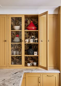 an open cabinet in the middle of a kitchen with marble counter tops and yellow cabinets