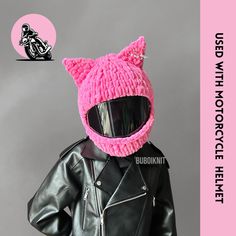 a pink knitted cat hat on top of a black leather jacket and motorcycle helmet