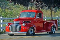 an old red truck is parked on the side of the road in front of a white fence