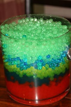 a bucket filled with green and blue beads on top of a wooden table