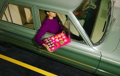 a woman sitting in the passenger seat of a green car holding a pink purse with sushi on it