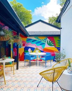 an outdoor dining area with colorful chairs and tables painted on the side of a building