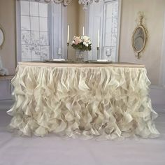 a table covered in ruffled cloth with candles and flowers on the table next to it