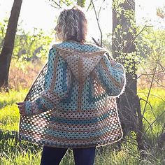 a woman standing in the woods wearing a crocheted jacket