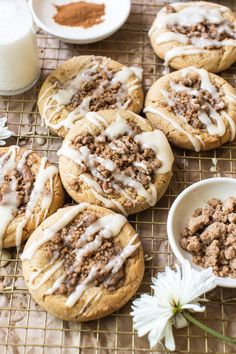 several cookies with white icing on a cooling rack next to some flowers and a glass of milk