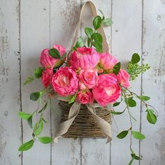 pink flowers in a basket hanging on a white wooden wall with green leaves and branches