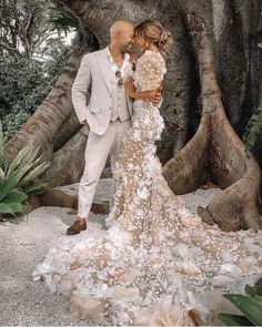 a man and woman standing next to each other in front of a tree with petals on it