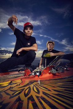 two young men sitting on top of skateboards in front of a blue cloudy sky