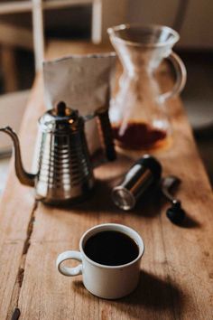 a cup of coffee sitting on top of a wooden table next to a metal pitcher