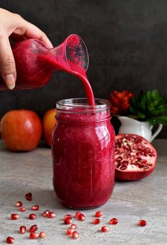 a person pouring red liquid into a jar with pomegranates around it